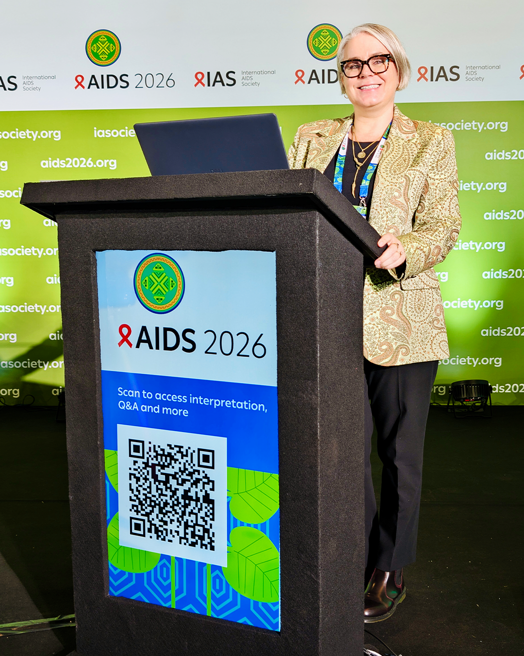 Sabrina Cluesman posing at a podium that reads AIDS 2026.