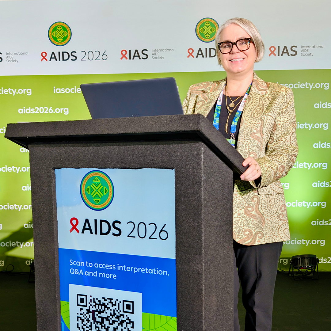 Sabrina Cluesman posing at a podium that reads AIDS 2026.