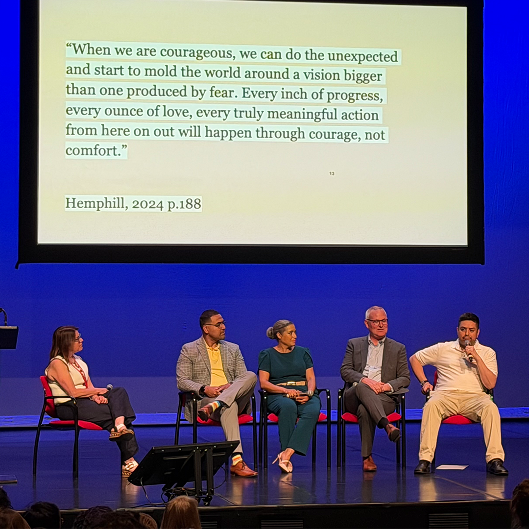 A panel speaking on stage in front of a projected screen